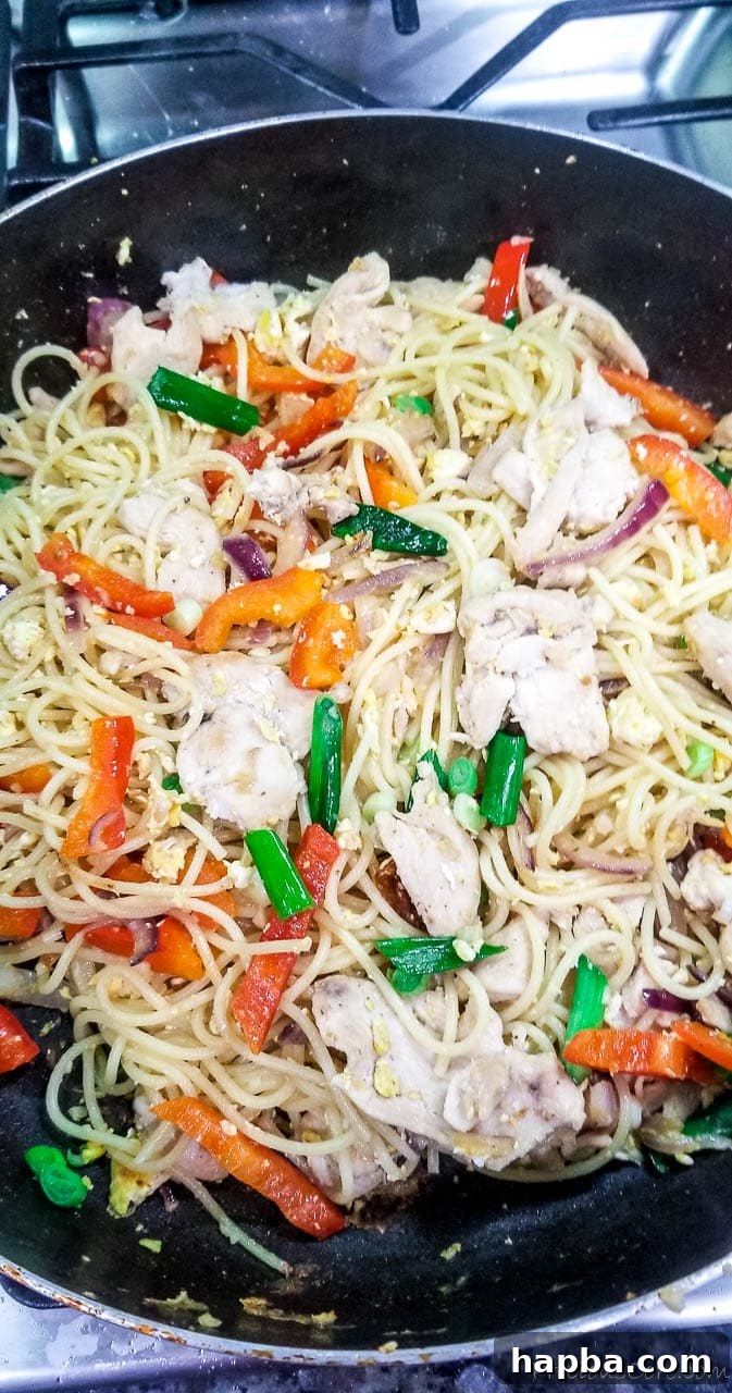 A vibrant spaghetti stir fry with chicken and vegetables, freshly prepared in a large wok or pan, showcasing its rich colors and appetizing texture.