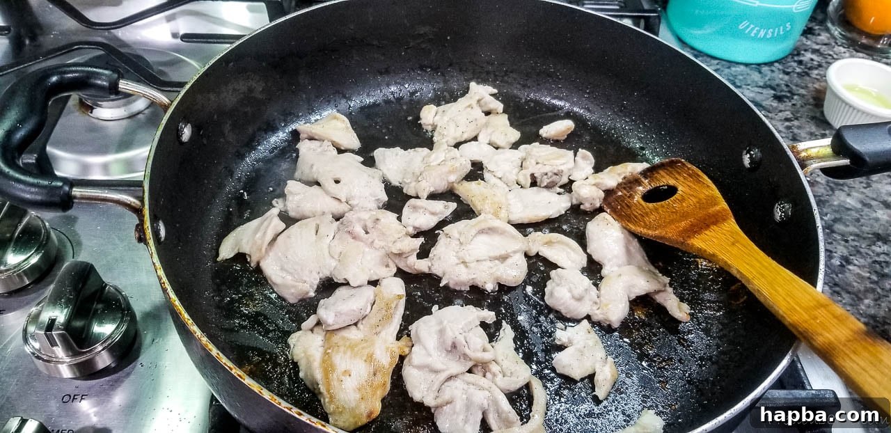 Thinly sliced chicken breast cooking in a hot pan, browning nicely as it stirs in preparation for the stir fry.