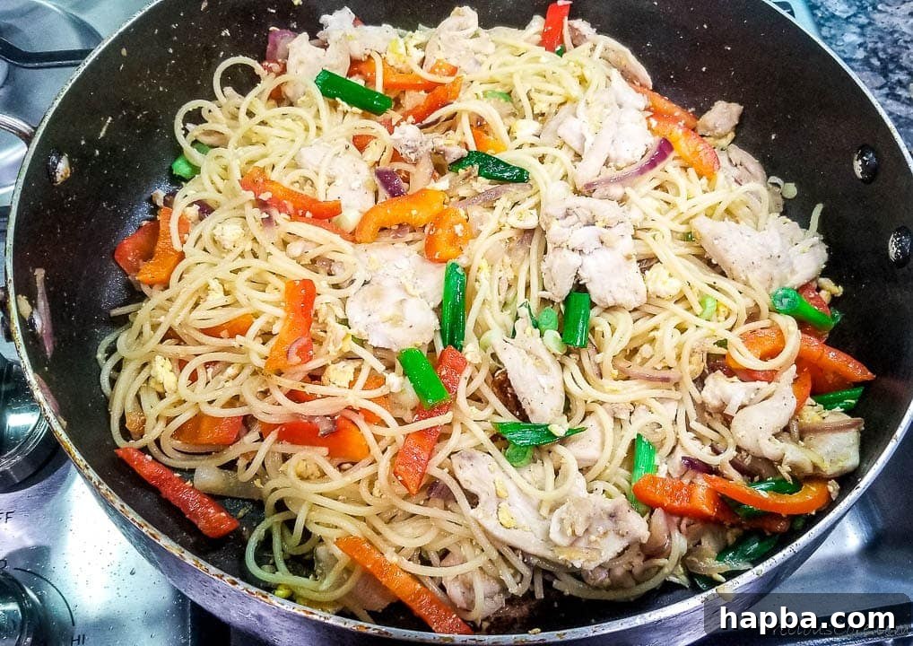 The spaghetti, chicken, and colorful vegetables being tossed together in a large wok, illustrating the final stages of the stir fry preparation.