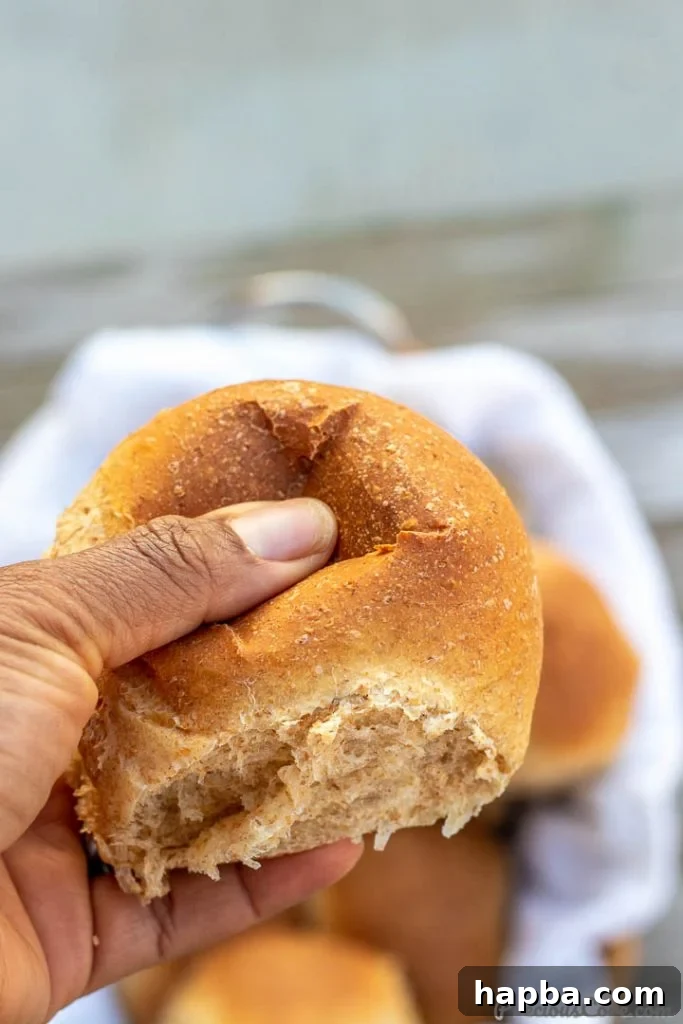 A hand gently pressing down on a soft, freshly baked dinner roll, demonstrating its perfect, springy texture.