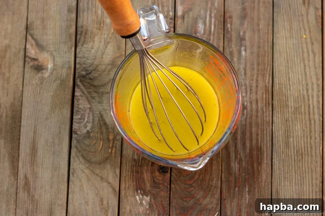 A simple yet elegant lemon vinaigrette in a clear measuring cup, showing its perfectly emulsified texture.