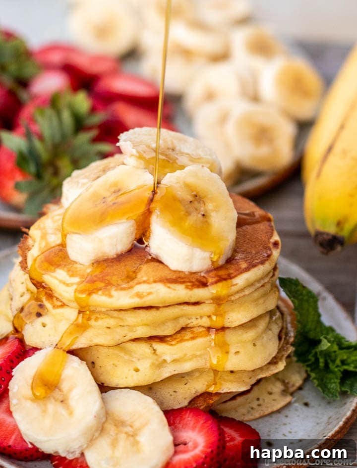 A tall stack of golden brown banana pancakes, generously topped with fresh banana slices and a luscious drizzle of maple syrup.