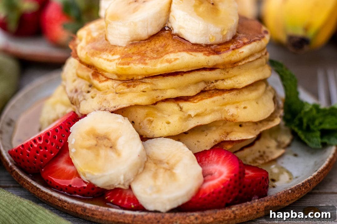 A close-up shot of fluffy banana pancakes on a plate, adorned with more sliced bananas and juicy strawberries, ready to be enjoyed.