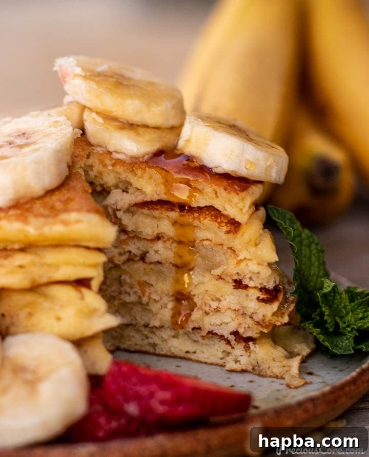 A close-up of a stack of banana pancakes, one cut open to reveal its fluffy interior, with warm maple syrup gracefully dripping down.