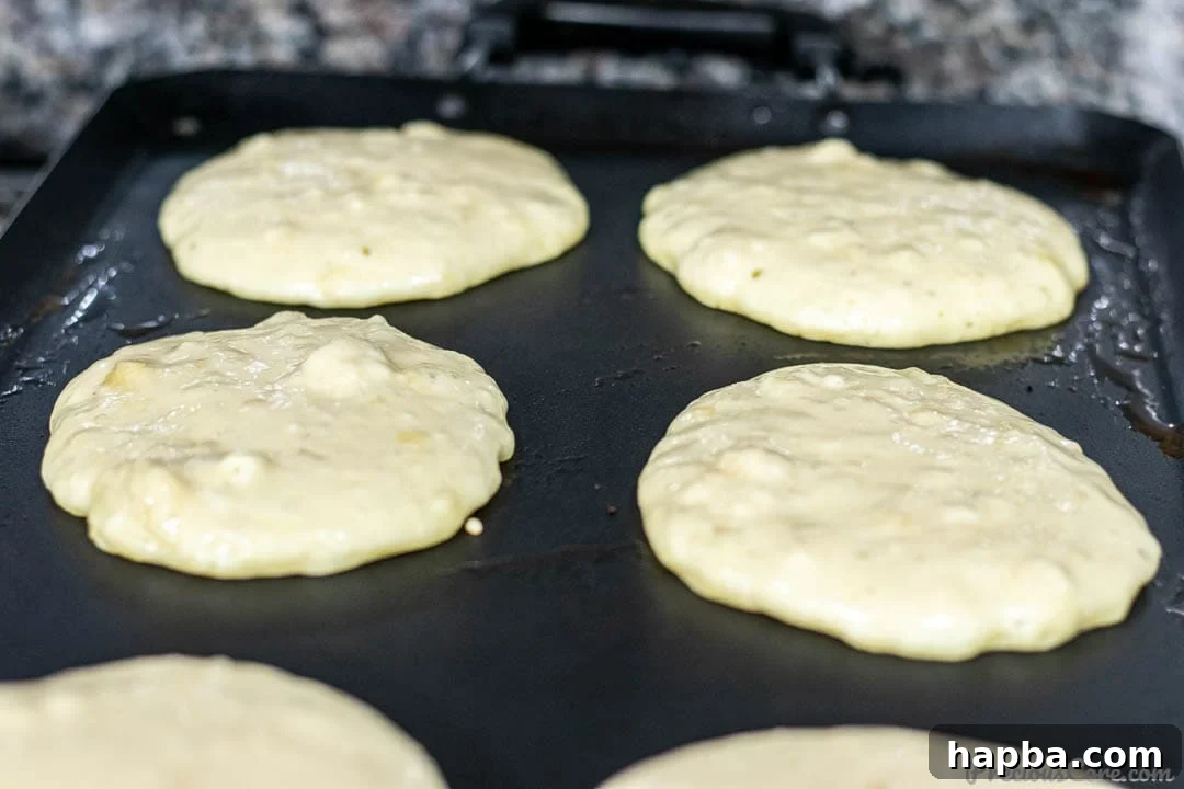 Banana pancake batter actively cooking and bubbling on a hot griddle, showing the process of becoming golden.