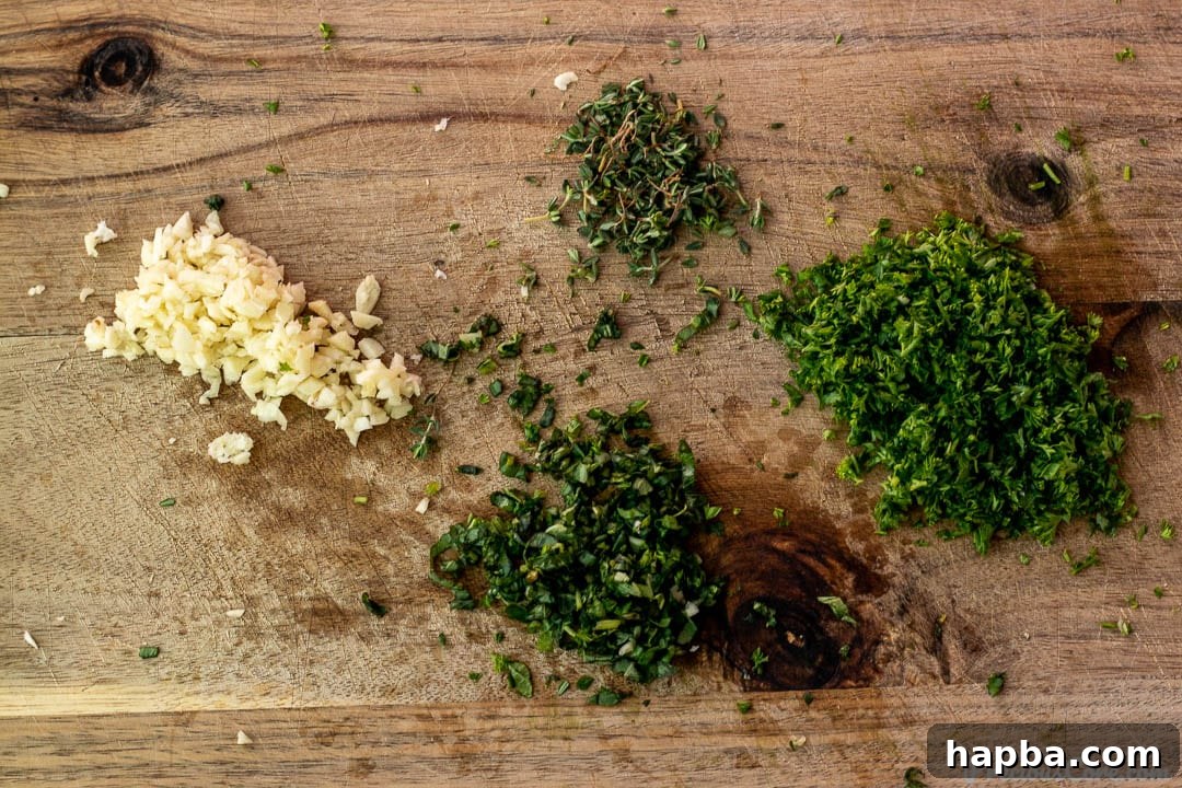 Freshly minced herbs (parsley, basil, thyme) and garlic cloves neatly arranged on a chopping board.