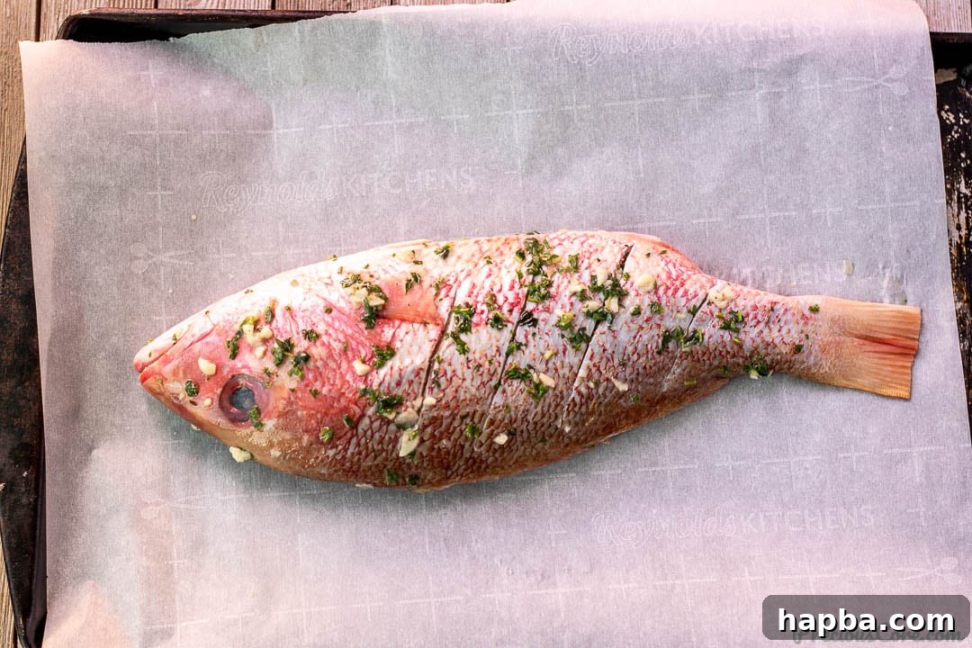 A whole red snapper, thoroughly coated and infused with the vibrant herb and garlic marinade.