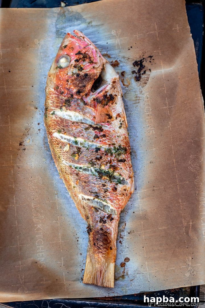An oven-grilled red snapper resting on a baking sheet, showcasing its perfectly crispy, golden-brown skin.