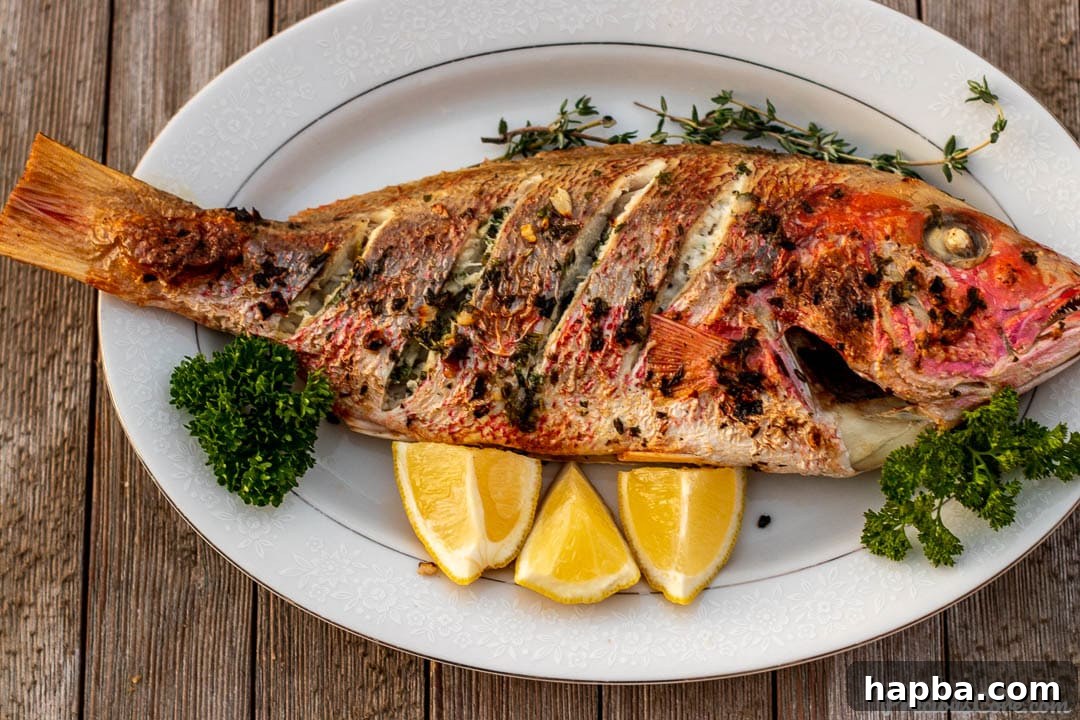 A magnificent oven-grilled whole red snapper presented on a platter, elegantly garnished with lemon slices and fresh herbs.