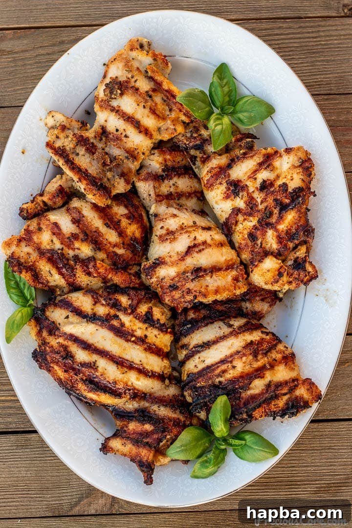 Grilled boneless chicken thighs on a platter with fresh herbs