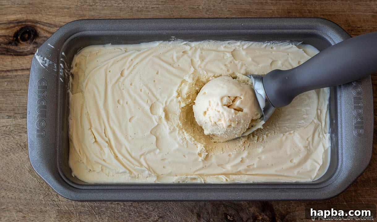Homemade vanilla ice cream beautifully setting in a loaf pan, covered with plastic wrap, ready for the freezer.