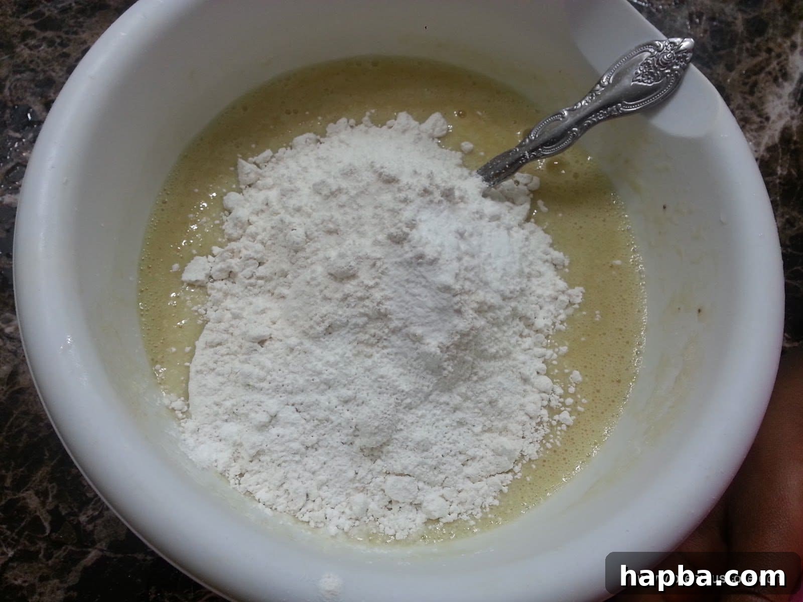 A mound of dry ingredients (flour, sugar, leavening agents) resting on top of the wet banana mixture in a bowl.