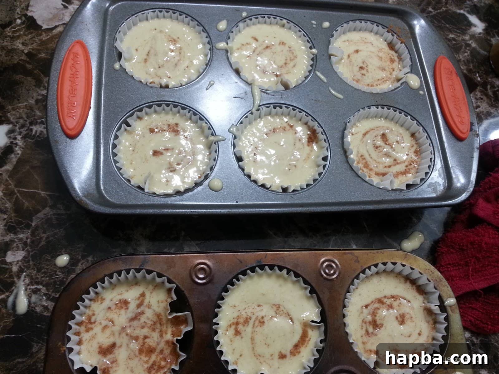 Muffin pan filled with banana cake batter, featuring an artistic swirl of cinnamon on each top.