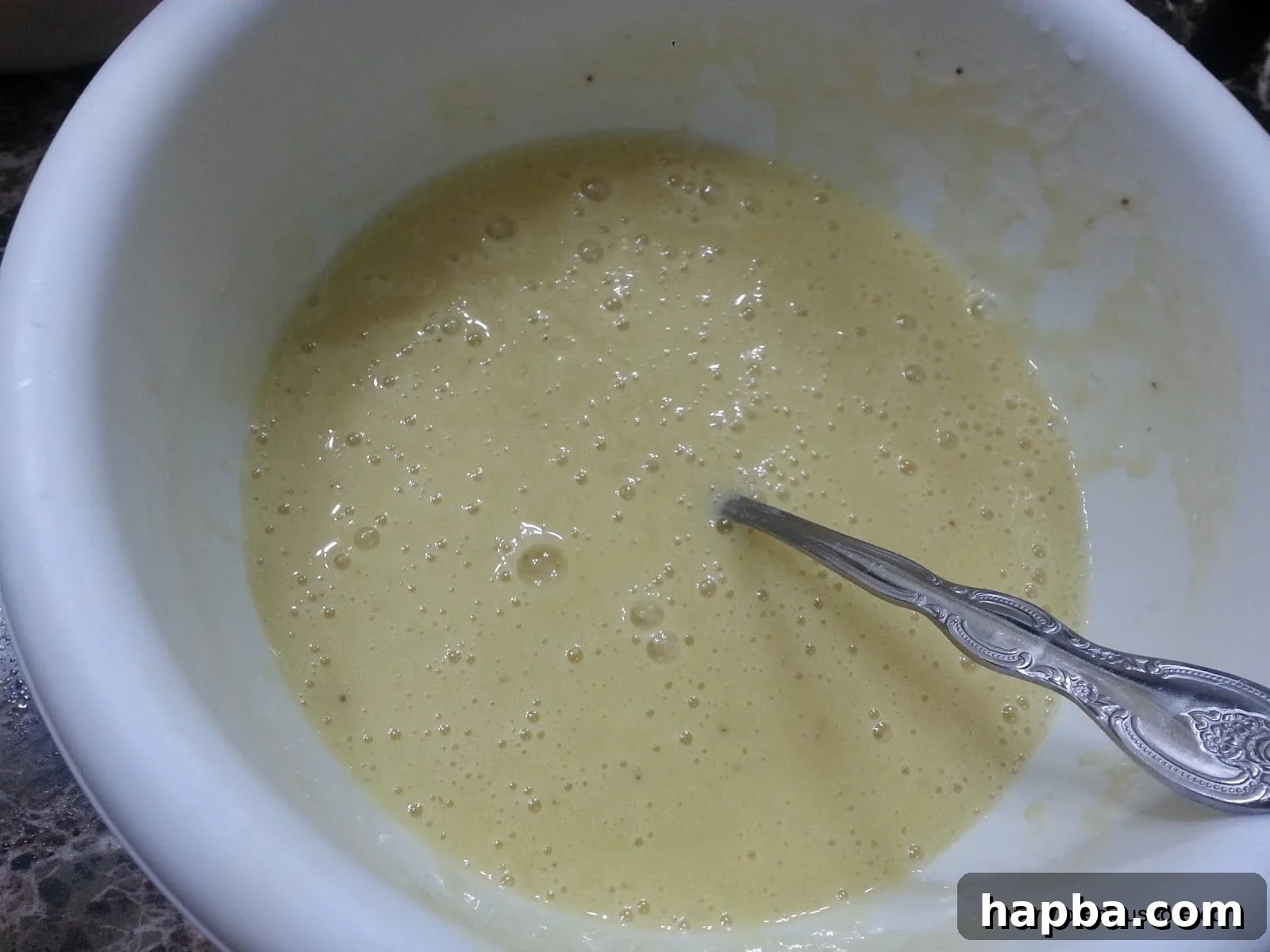 A spoon stirring a bowl of thoroughly mixed wet ingredients for banana cake.
