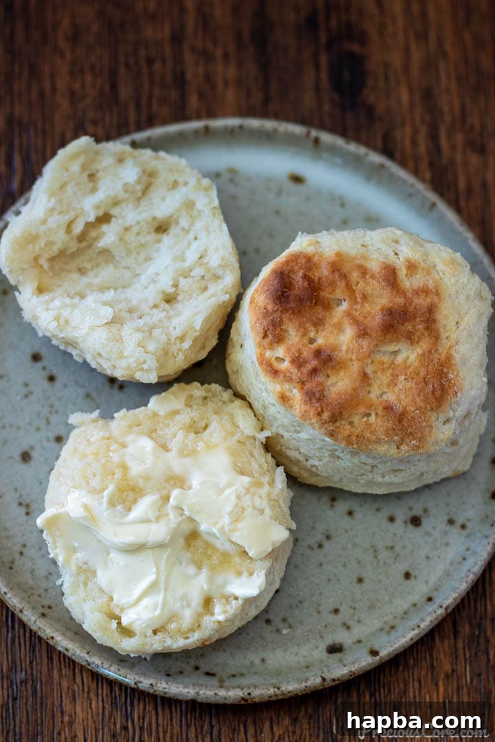 A stack of warm cream cheese biscuits, one with butter generously spread on top, ready for breakfast.