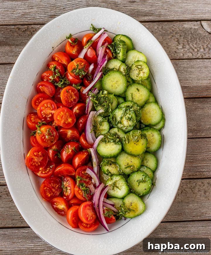 Vibrant Cucumber, Tomato, and Onion Medley 2 A beautifully arranged cucumber tomato onion salad on a white platter, glistening with dressing.