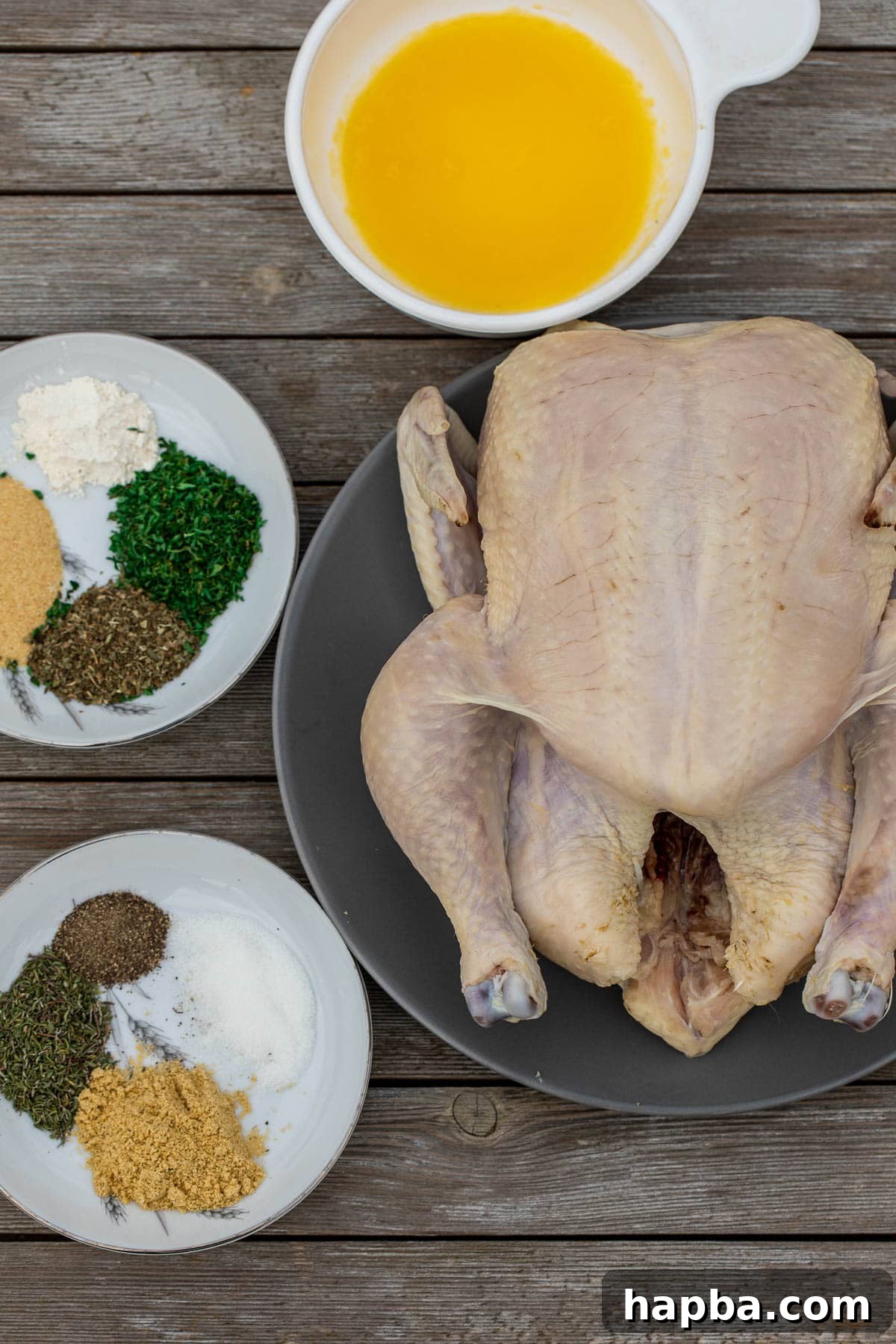 Succulent Herb Roasted Chicken 4 A whole raw chicken, a selection of vibrant dried spices and fragrant fresh herbs, and essential seasoning artfully laid out on a rustic wooden board, ready for preparation.