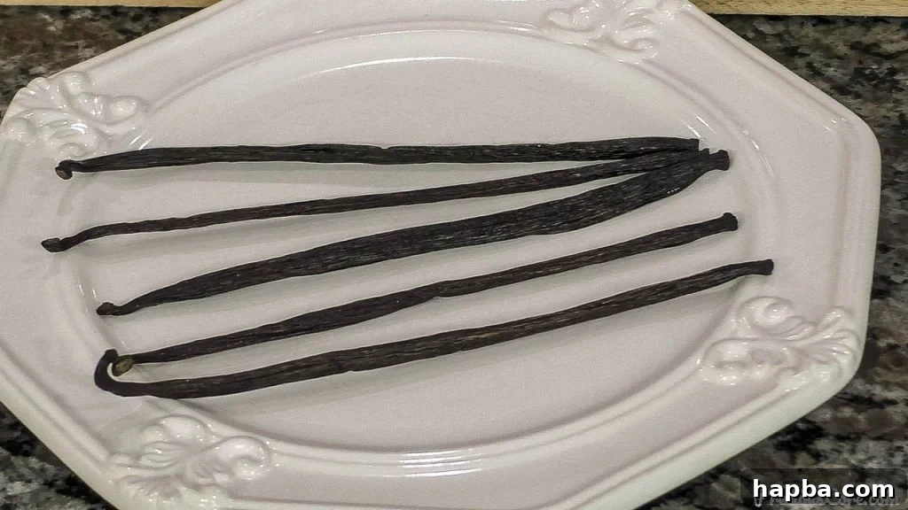 Pure Vanilla Perfection From Your Kitchen 3 Close-up of grade B Tahitian vanilla beans lying on a white plate, showcasing their dark, wrinkled texture and rich aroma.