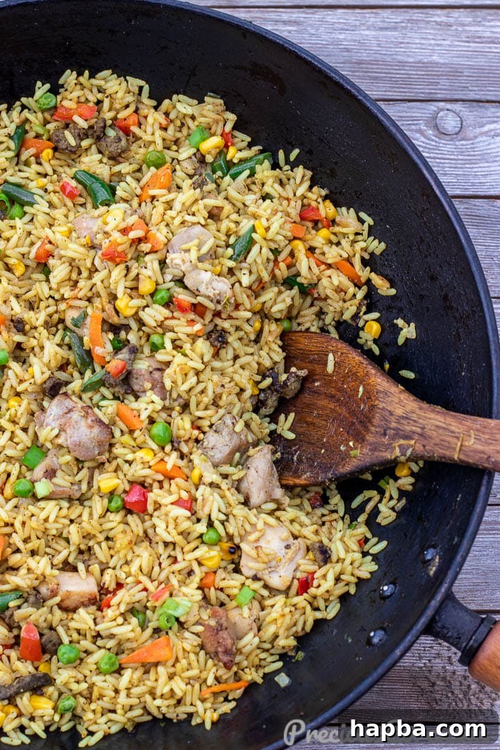 Close-up of African Chicken Fried Rice sizzling in a large wok with a spatula