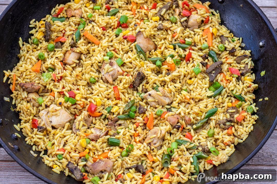 Large wok brimming with African Fried Rice, showing pieces of chicken and liver among the colorful vegetables