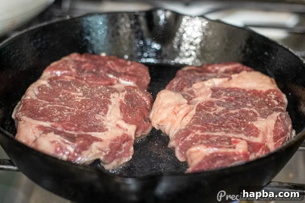 A raw ribeye steak sizzling as it begins to sear in a hot cast iron skillet.