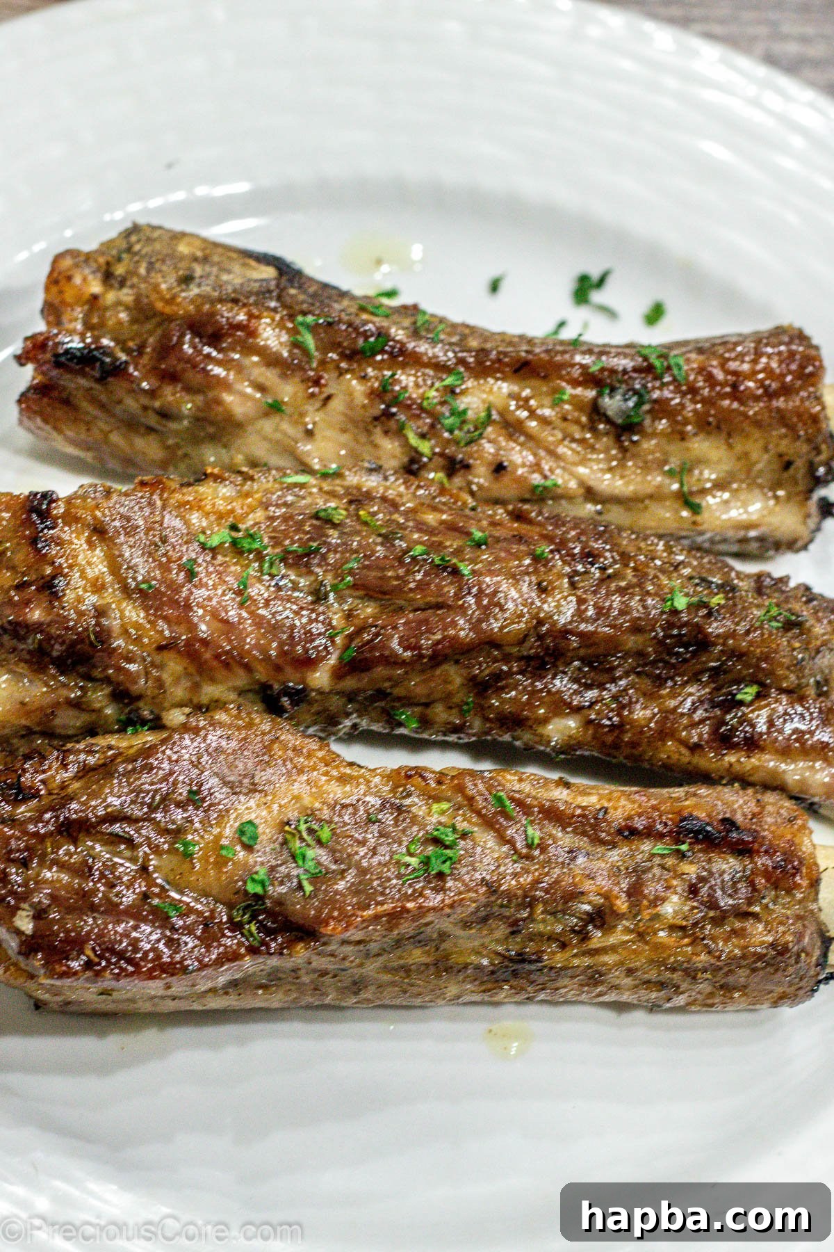 Tender Dry-Rubbed Ribs 2 Three perfectly baked dry rub ribs resting on a pristine white plate, garnished for serving.