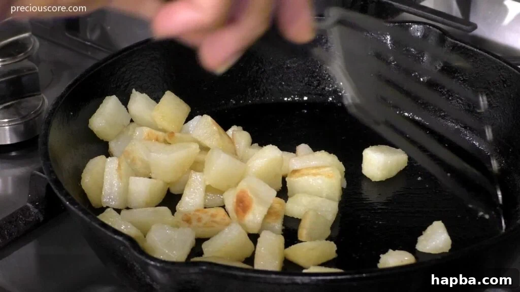 Hearty Potato Egg Bake 7 Diced and cooked potatoes sizzling and turning golden brown in a hot skillet, showing crispy edges.