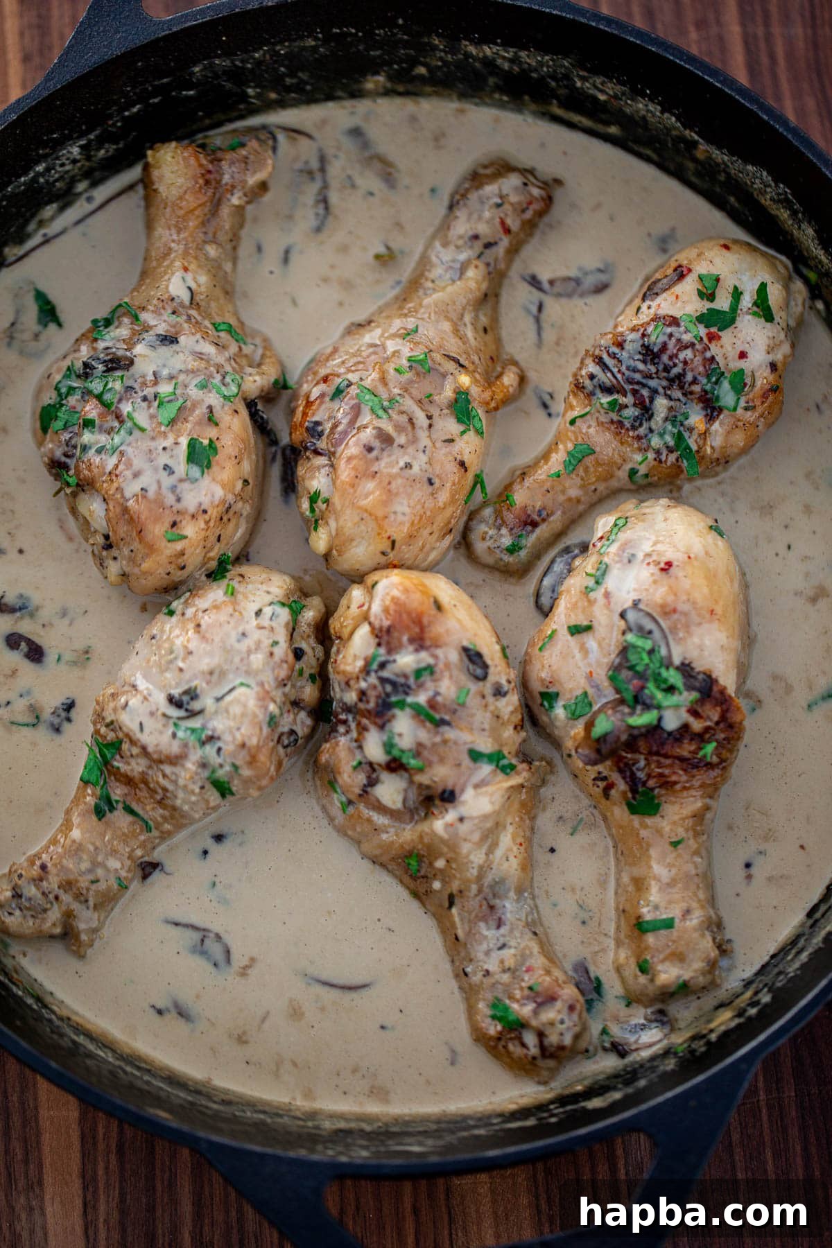 Succulent chicken drumsticks in a rich, creamy mushroom sauce, served in a rustic cast iron skillet.