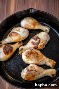 Browned chicken drumsticks sizzling in a cast iron skillet, ready for the sauce.