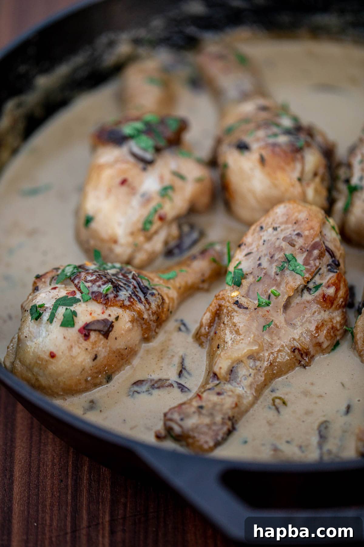 A tantalizing overhead shot of creamy chicken drumsticks in a skillet, garnished with fresh parsley.