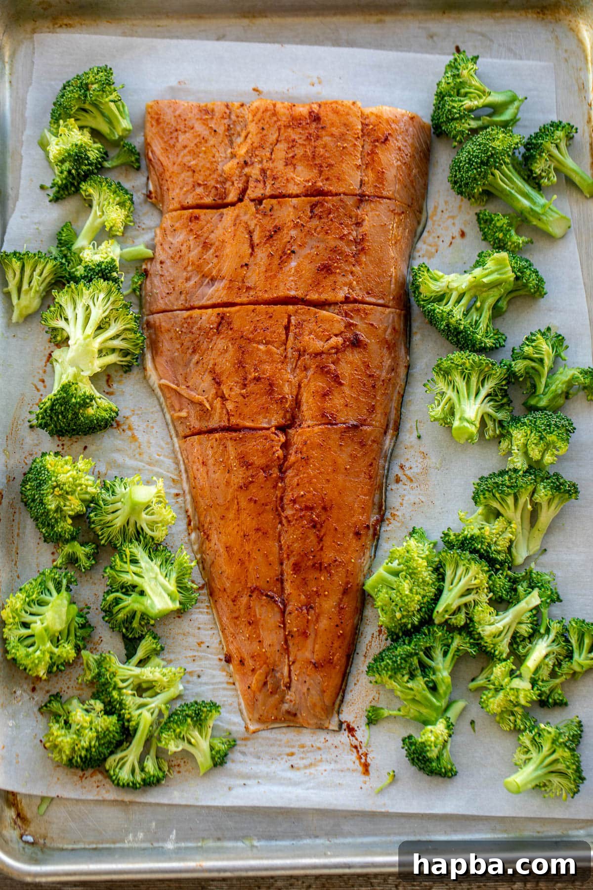 Effortless Sheet Pan Salmon and Broccoli 5 Seasoned salmon fillets and broccoli florets arranged on a parchment-lined sheet pan