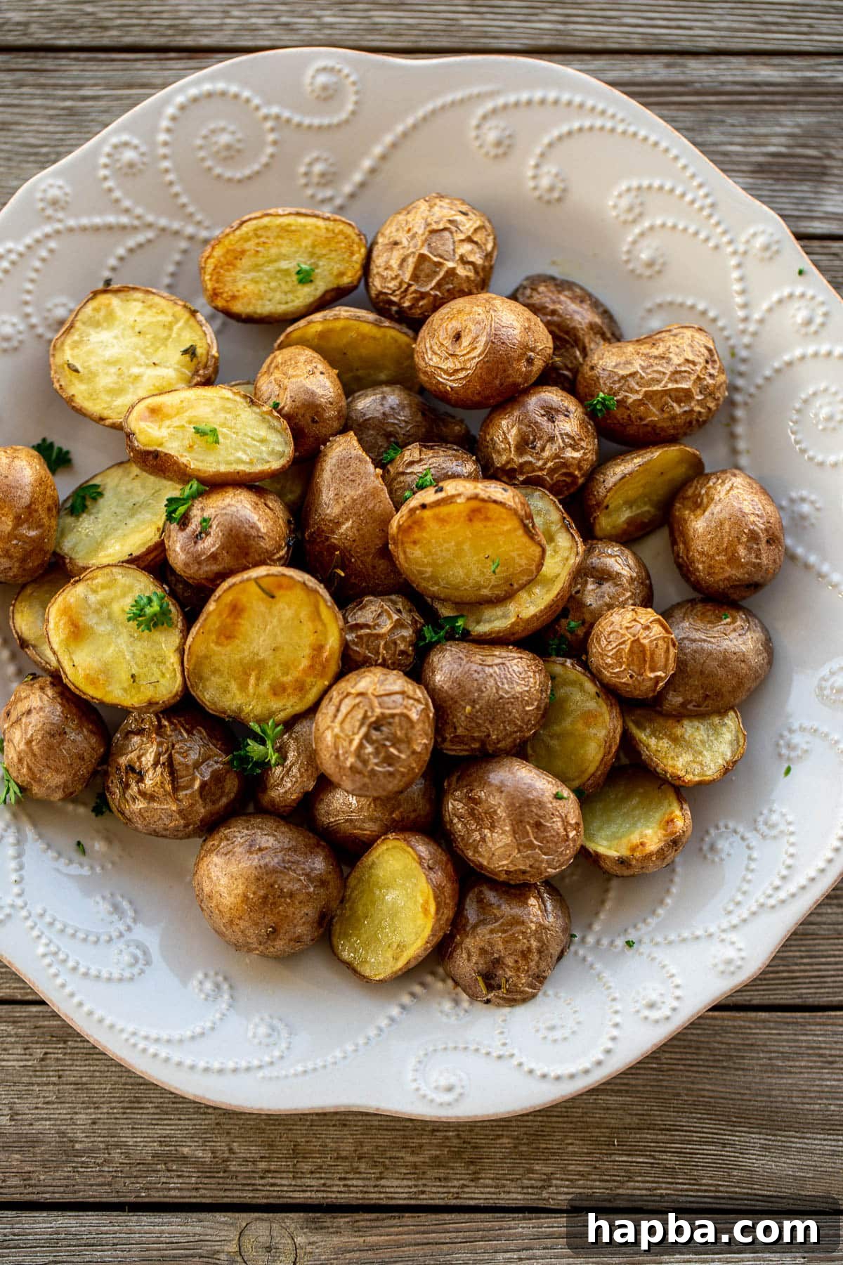 Large plate of beautifully golden-brown oven roasted baby potatoes, garnished with fresh herbs