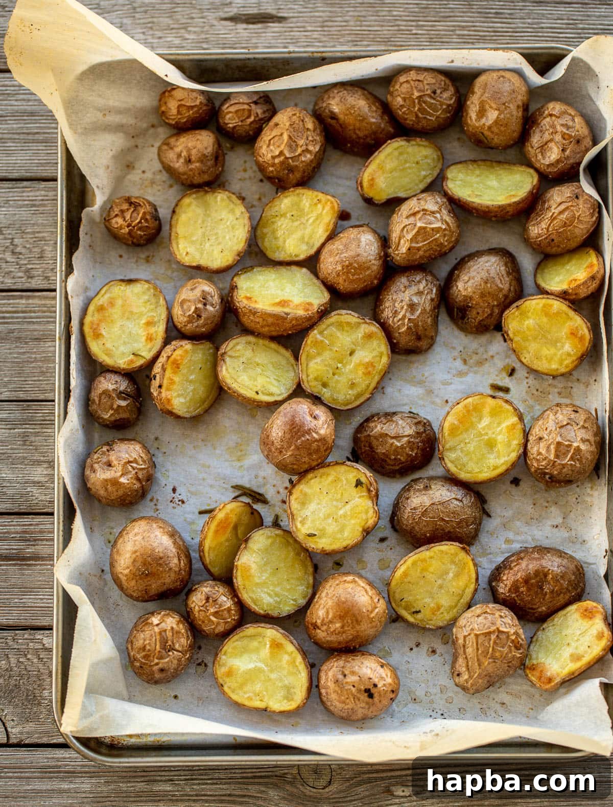Baby potatoes coated in herbs and oil, laid out on a baking sheet lined with parchment paper, ready for roasting