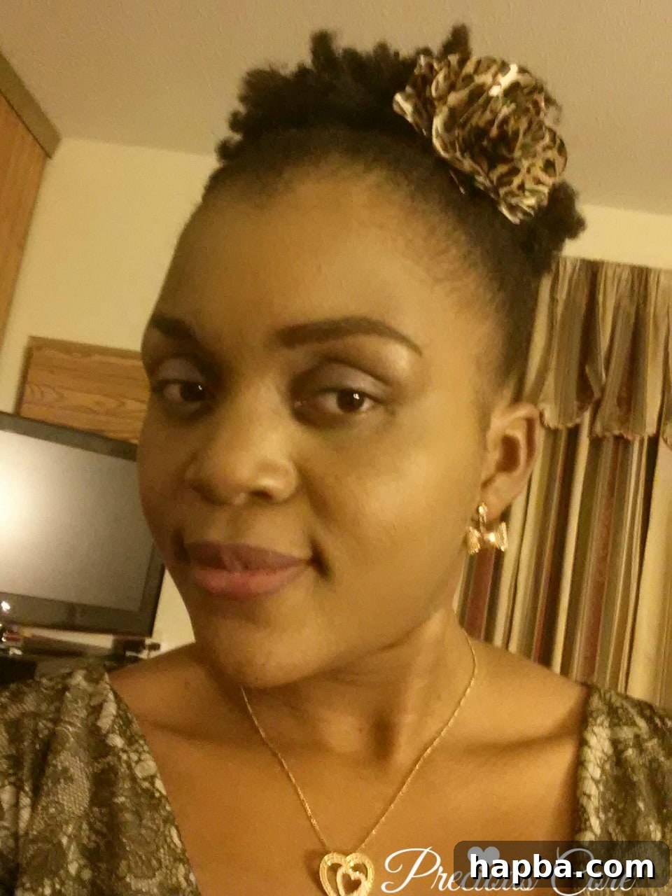 A woman smiling, showcasing her natural hair styled in a high puff with laid edges.