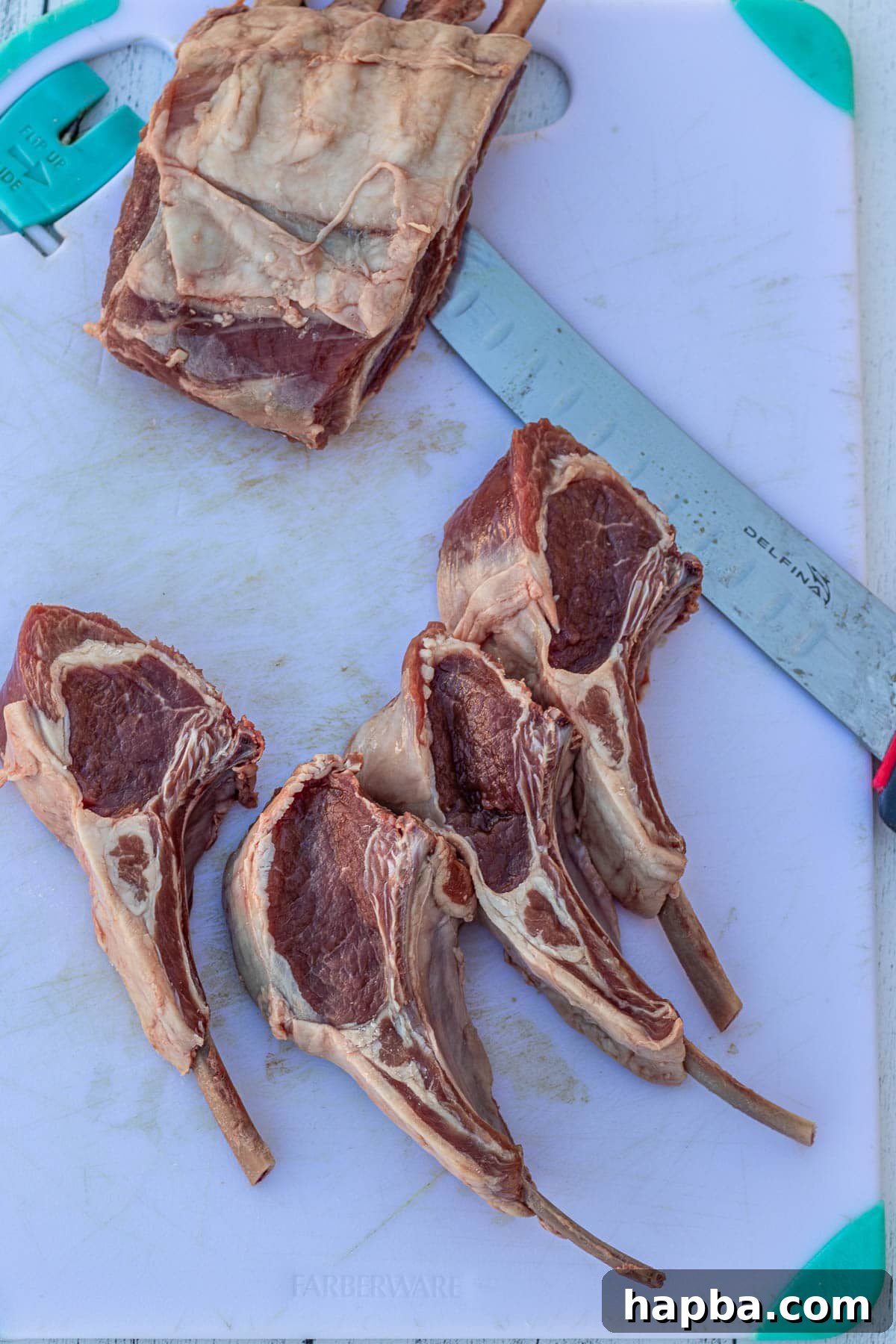 A chef's knife carefully cutting a rack of lamb into individual chops on a wooden chopping board.
