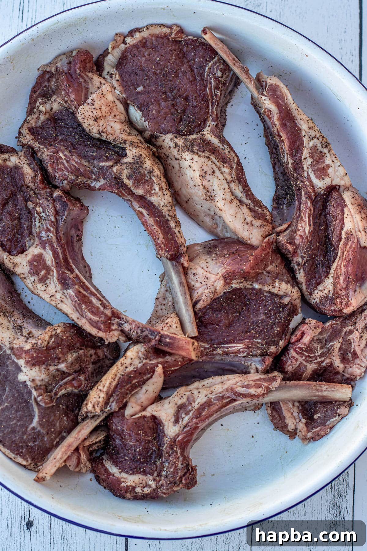 Seasoned lamb chops resting in a white ceramic bowl, ready for searing.