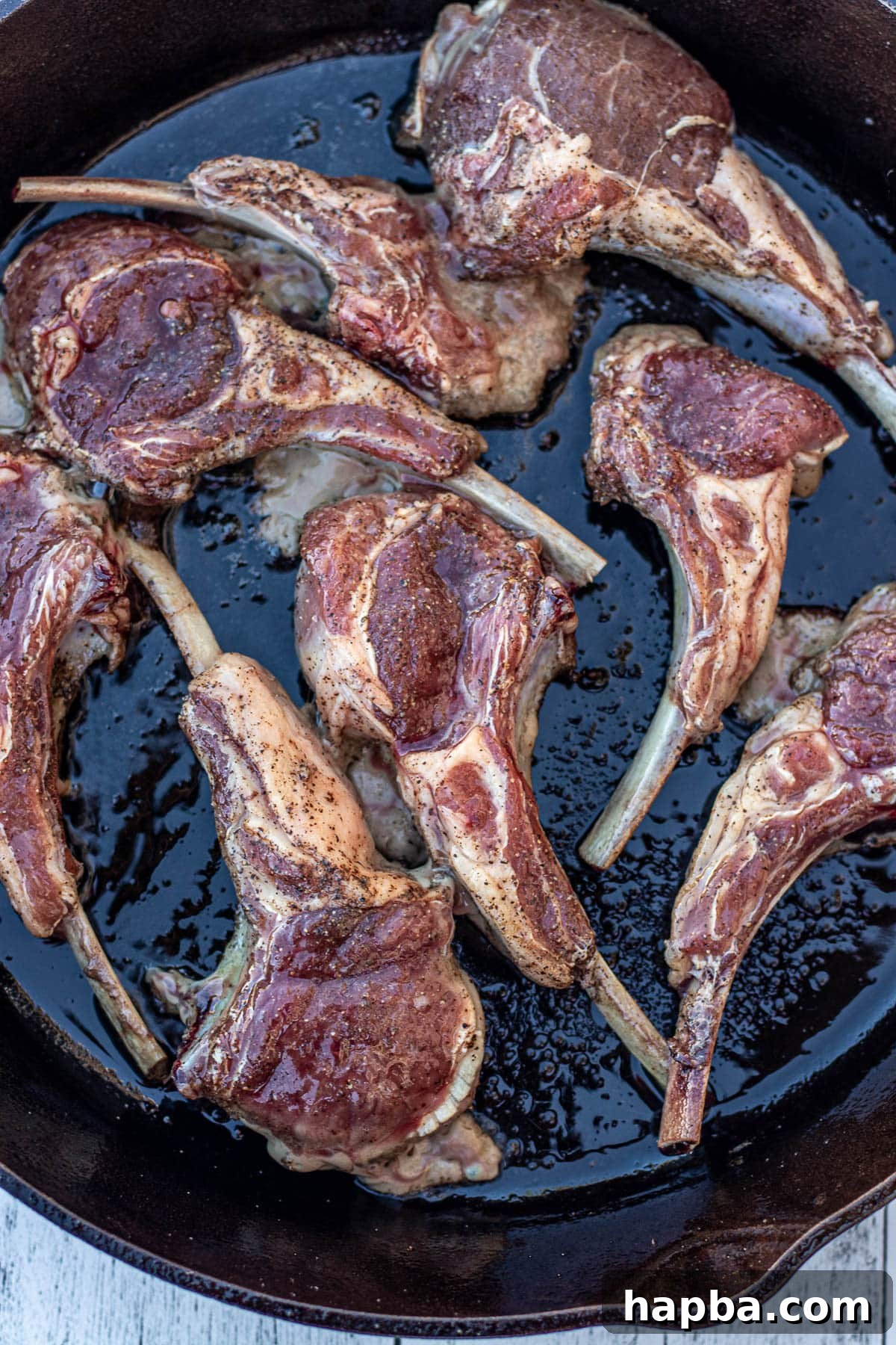 Lamb chops being carefully placed into a hot cast iron skillet, starting the searing process.