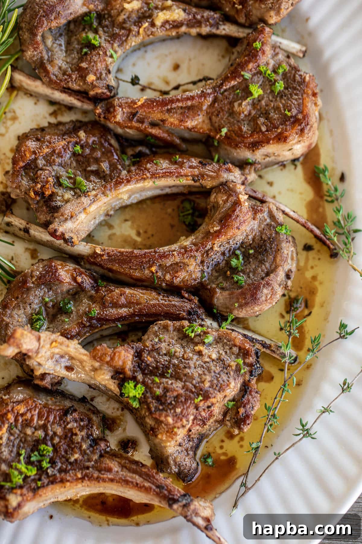 Perfectly pan seared lamb chops served on a large tray, garnished elegantly with fresh thyme and rosemary leaves.