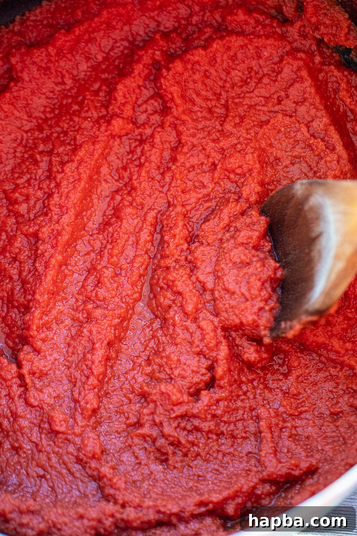 Artisan Homemade Tomato Paste 8 Thickening tomato puree reducing in a large pot on the stove, transforming into paste
