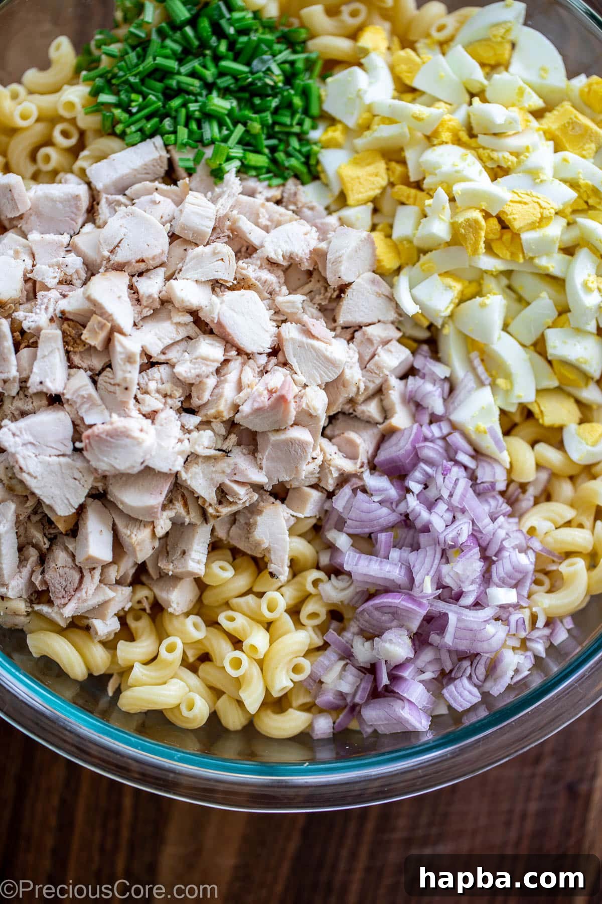 Creamy Chicken Macaroni Delight 5 A large mixing bowl containing all the salad ingredients: cooked macaroni, diced chicken, chopped eggs, celery, and red onions.