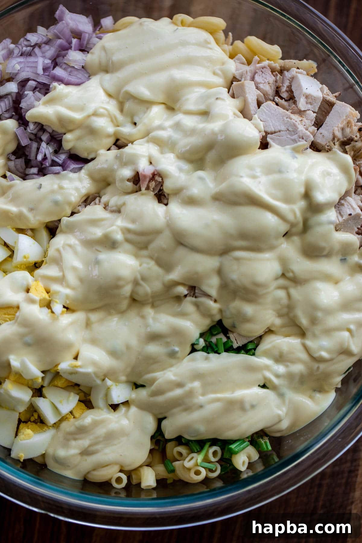Creamy Chicken Macaroni Delight 7 The creamy dressing being poured over the assembled salad ingredients in the large bowl.
