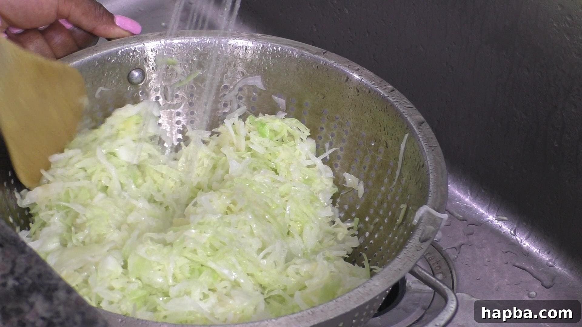 Blanched cabbage being rinsed with cold water in a colander, stopping the cooking process.