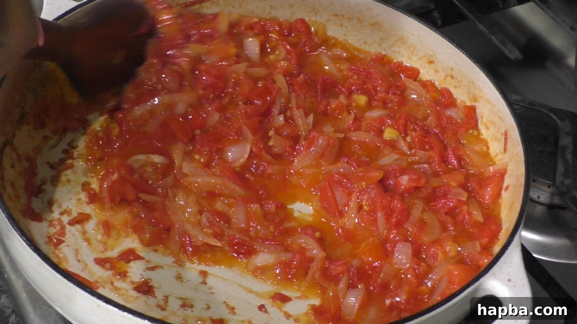 Chopped tomatoes and onions cooking down in a pot, forming the aromatic base of the stew.