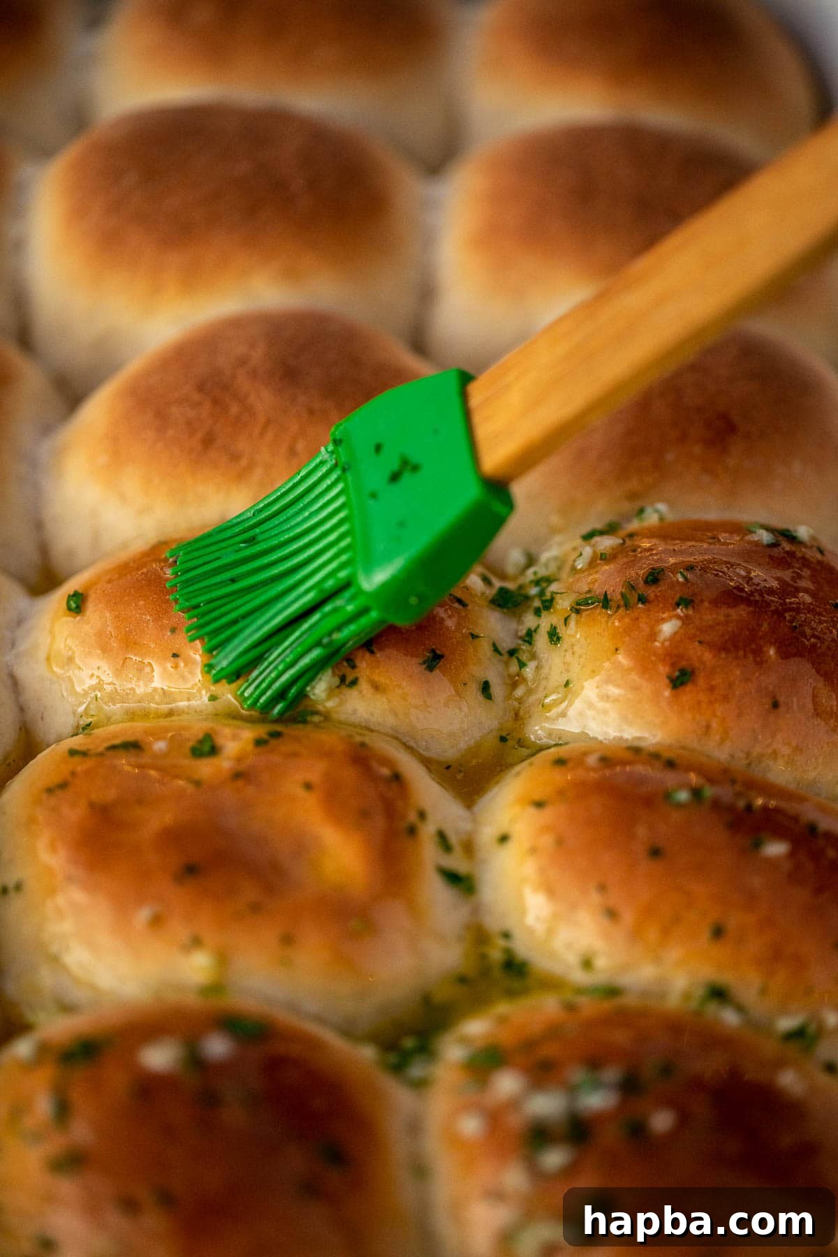 A pastry brush applies the fragrant garlic butter over the warm dinner rolls.