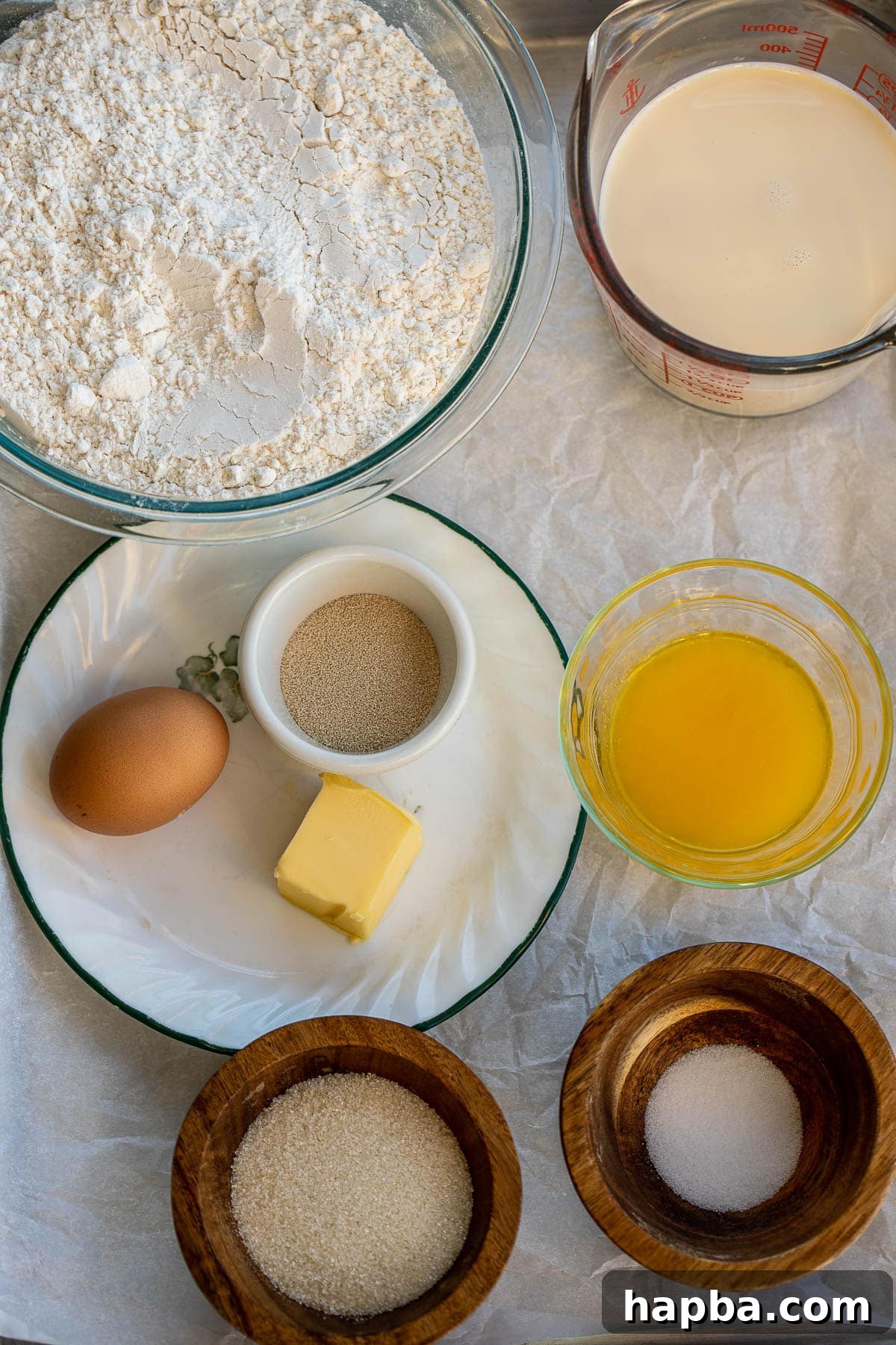 A selection of raw ingredients for dinner rolls laid out on a kitchen counter, including flour, sugar, yeast, milk, and eggs.