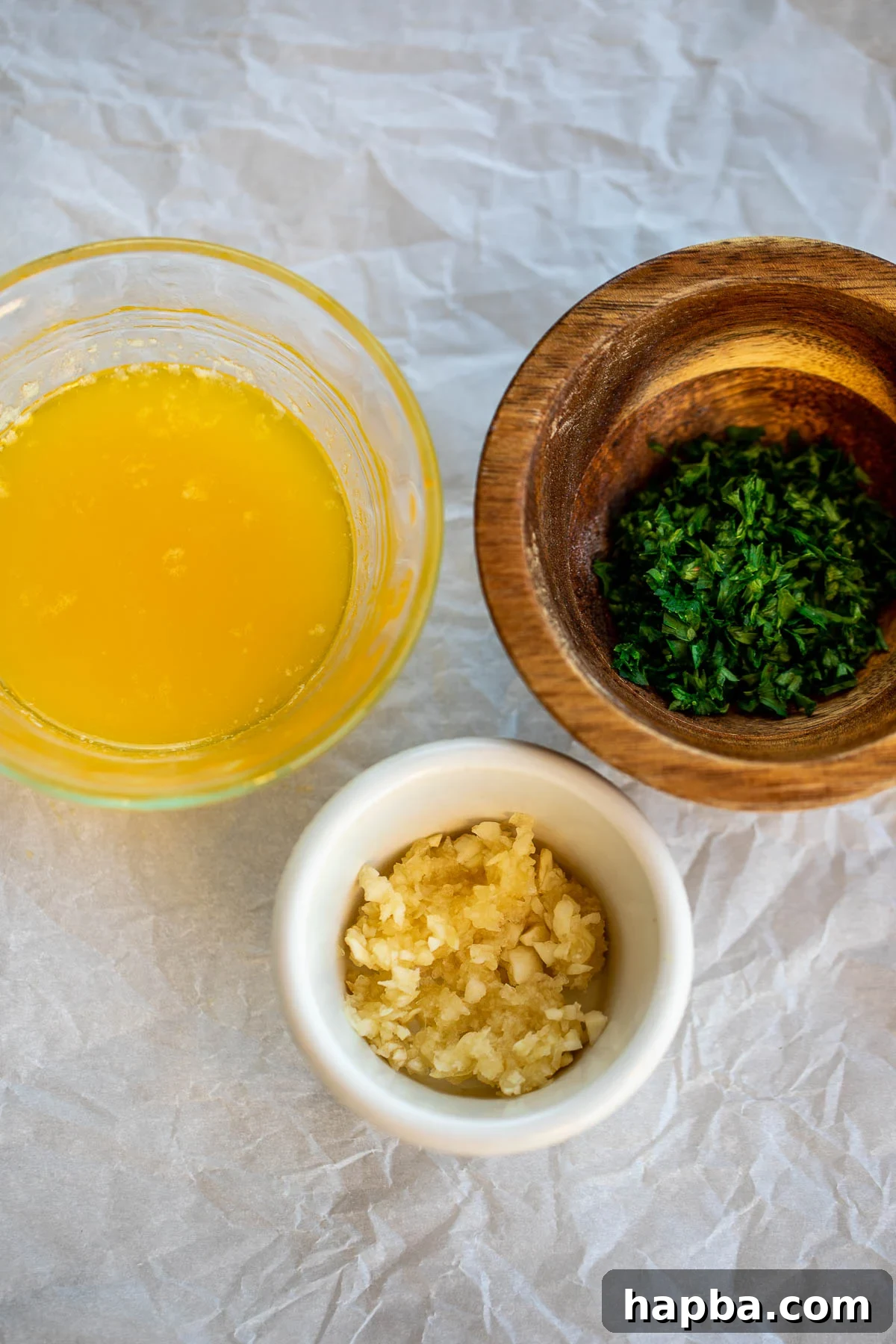 Minced garlic, melted butter, and fresh parsley are neatly arranged as ingredients for the garlic butter topping.