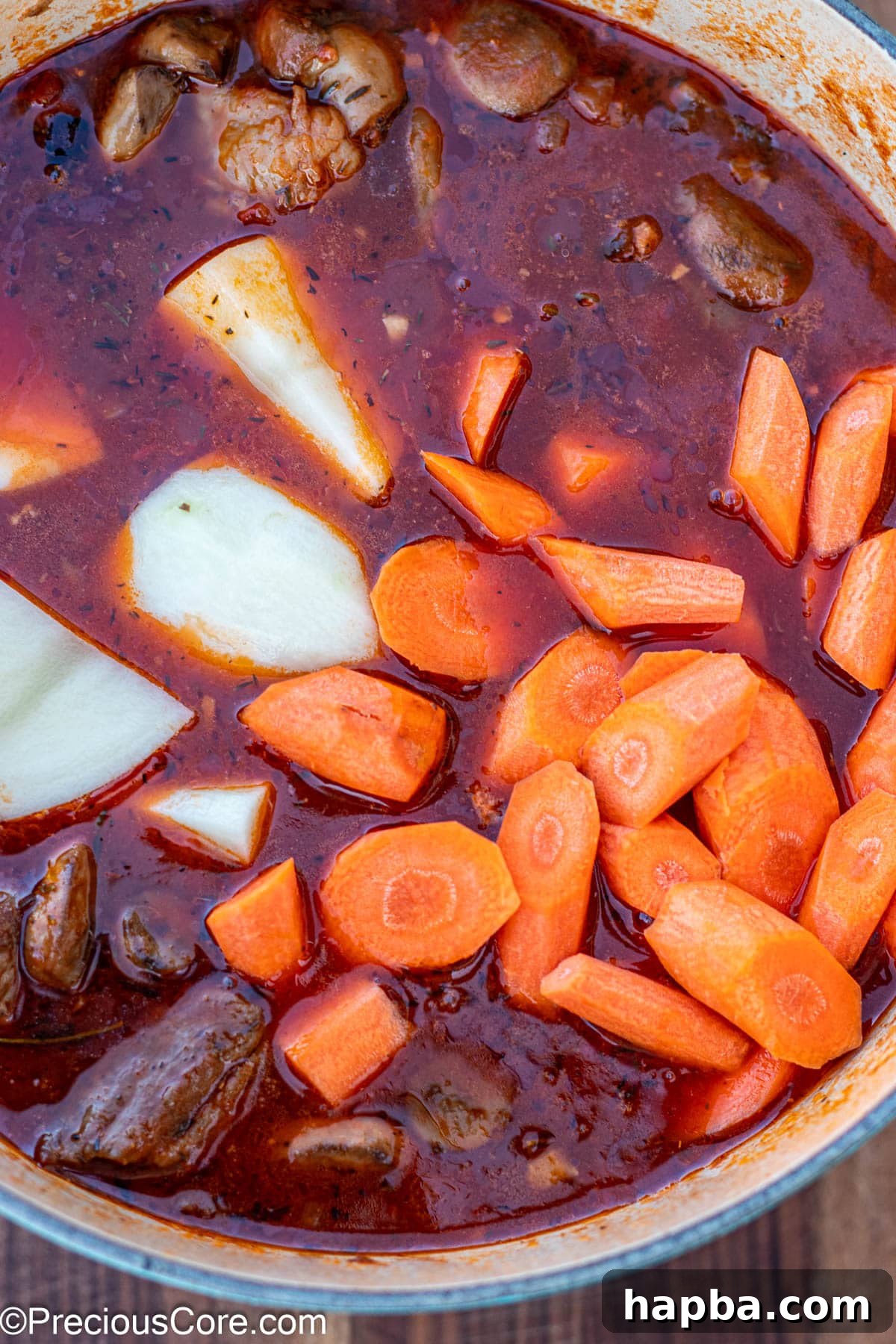 Non-Alcoholic Beef Stew 11 Raw carrots and potatoes freshly added to a pot of simmering beef stew.