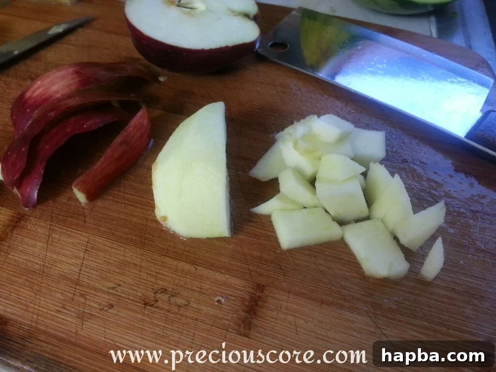 The last ingredient, diced apple, being gently mixed into the large bowl already brimming with a colorful assortment of tropical fruits.