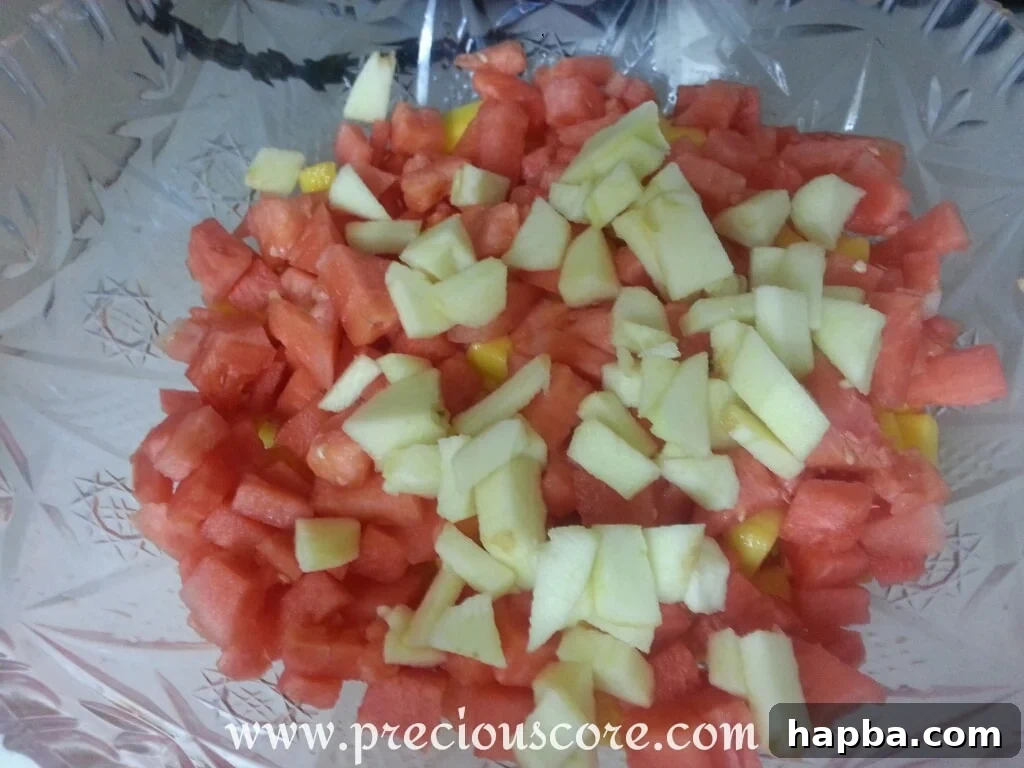 A large, clear bowl filled with the completed tropical fruit salad, featuring an appealing mix of pineapple, papaya, mango, watermelon, and apple pieces, ready to be served.