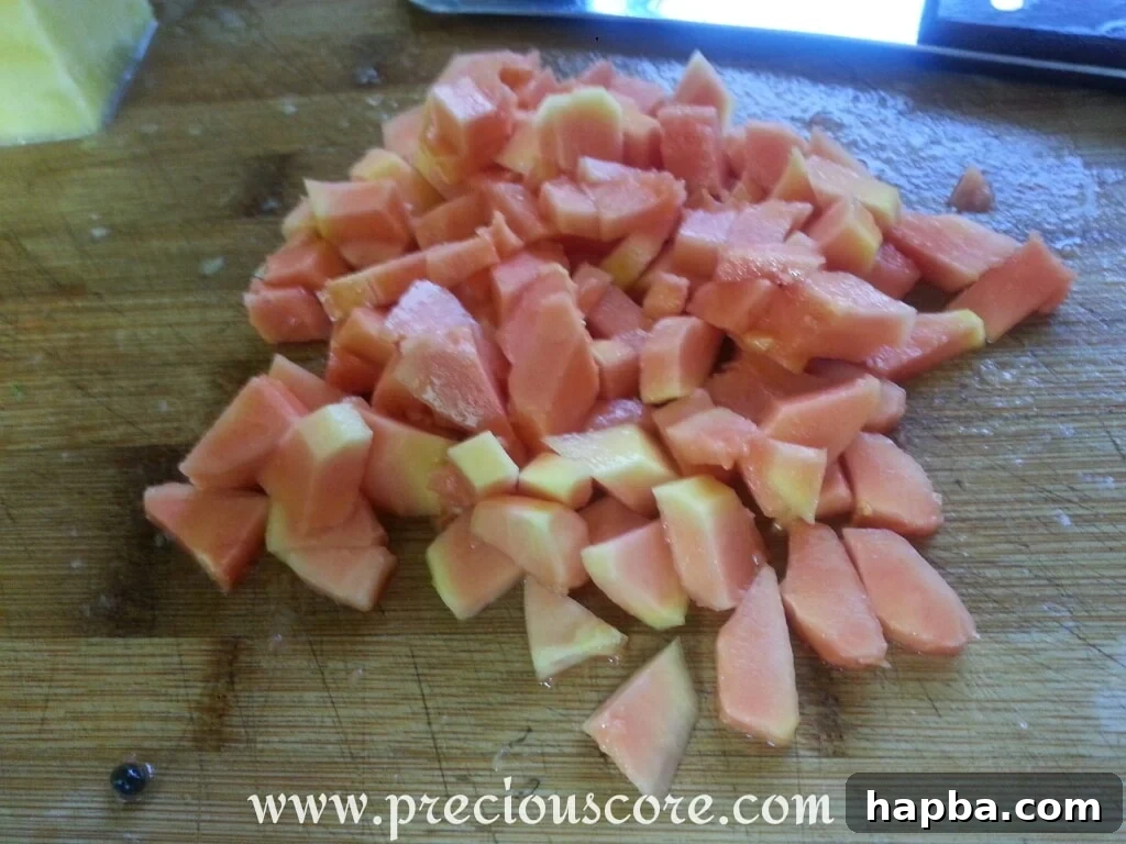 Two ripe mangoes, one partially peeled, being cut around its large, flat seed on a cutting board.